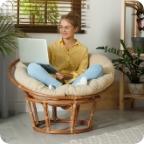 Woman sits with laptop in comfortable round basket lounge chair.